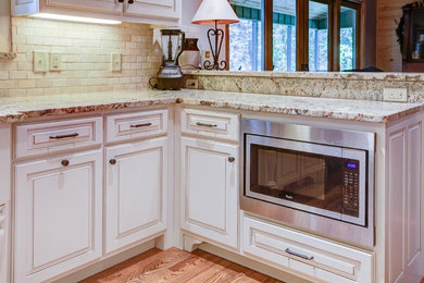 Kitchen - medium tone wood floor kitchen idea in Atlanta with a farmhouse sink, raised-panel cabinets, beige cabinets, granite countertops, beige backsplash, stone tile backsplash and stainless steel appliances