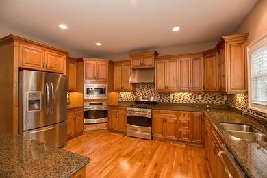 Enclosed kitchen - large traditional u-shaped medium tone wood floor and brown floor enclosed kitchen idea in Other with a double-bowl sink, raised-panel cabinets, medium tone wood cabinets, granite countertops, multicolored backsplash, mosaic tile backsplash, stainless steel appliances, an island and brown countertops