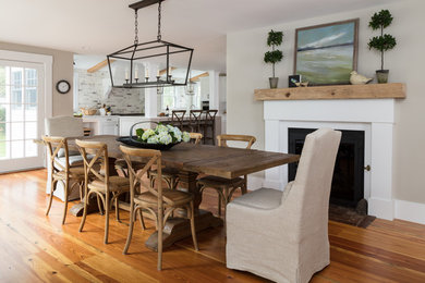 Design ideas for a mid-sized country kitchen/dining combo in Boston with beige walls, medium hardwood floors, a standard fireplace, a plaster fireplace surround and brown floor.