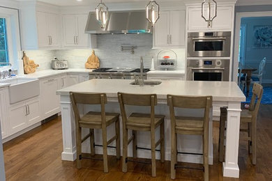 Kitchen pantry - large traditional l-shaped medium tone wood floor and brown floor kitchen pantry idea in Boston with a farmhouse sink, shaker cabinets, white cabinets, quartz countertops, gray backsplash, stainless steel appliances, an island and white countertops
