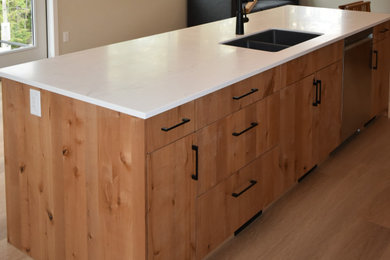 Minimalist beige floor kitchen photo in Vancouver with an undermount sink, flat-panel cabinets, medium tone wood cabinets, solid surface countertops, stainless steel appliances and an island