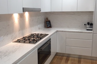 This is an example of a modern l-shaped eat-in kitchen in Sydney with marble benchtops, white splashback, stone slab splashback, flat-panel cabinets, white cabinets, stainless steel appliances and with island.