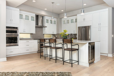 Design ideas for a large transitional l-shaped separate kitchen in Seattle with an undermount sink, shaker cabinets, white cabinets, marble benchtops, grey splashback, stone tile splashback, stainless steel appliances, light hardwood floors, with island and beige floor.