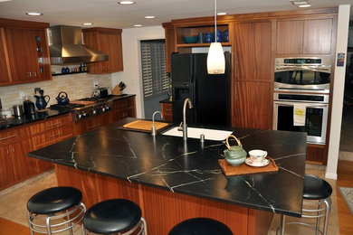 Inspiration for a mid-sized modern limestone floor kitchen remodel in Los Angeles with a drop-in sink, medium tone wood cabinets, soapstone countertops, black appliances and an island