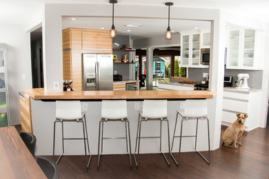 Inspiration for a mid-sized modern u-shaped eat-in kitchen in Milwaukee with a farmhouse sink, flat-panel cabinets, medium wood cabinets, granite benchtops, grey splashback, porcelain splashback, stainless steel appliances, dark hardwood floors, with island and brown floor.