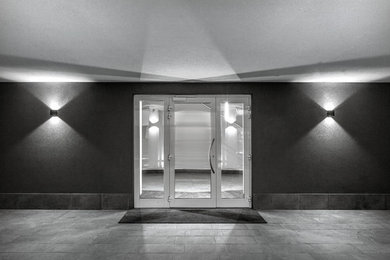 Ispirazione per un ingresso o corridoio minimalista con pareti grigie, una porta in vetro e pavimento grigio