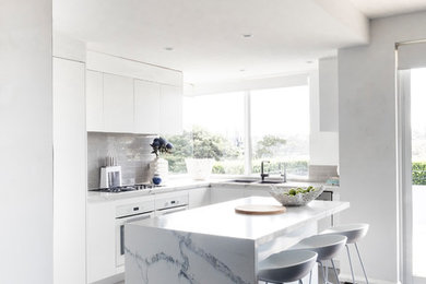 This is an example of a contemporary l-shaped kitchen in Sydney with an undermount sink, flat-panel cabinets, white cabinets, grey splashback, panelled appliances and white benchtop.