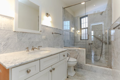 Inspiration for a mid-sized timeless 3/4 gray tile and porcelain tile porcelain tile alcove shower remodel in New York with shaker cabinets, white cabinets, a one-piece toilet, white walls, an undermount sink, marble countertops, a hinged shower door and gray countertops