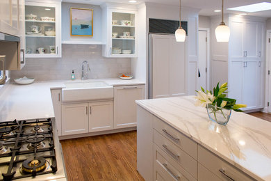 Inspiration for a large timeless u-shaped medium tone wood floor enclosed kitchen remodel in Kansas City with a farmhouse sink, shaker cabinets, white cabinets, quartz countertops, white backsplash, ceramic backsplash, paneled appliances, an island and white countertops