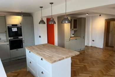 Medium sized modern l-shaped open plan kitchen in Sussex with a single-bowl sink, brown cabinets, wood worktops, black appliances, medium hardwood flooring, an island, brown floors and feature lighting.