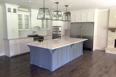 Example of a mid-sized transitional l-shaped dark wood floor and brown floor open concept kitchen design in Other with an undermount sink, shaker cabinets, white cabinets, quartz countertops, white backsplash, subway tile backsplash, stainless steel appliances and an island