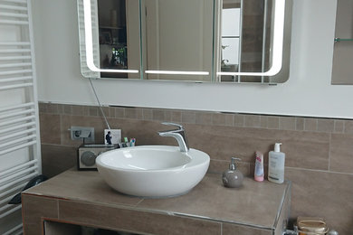 Mittelgroßes Modernes Badezimmer En Suite mit flächenbündigen Schrankfronten, braunen Schränken, Einbaubadewanne, bodengleicher Dusche, Wandtoilette, braunen Fliesen, Keramikfliesen, weißer Wandfarbe, Keramikboden, Aufsatzwaschbecken, gefliestem Waschtisch, braunem Boden und brauner Waschtischplatte in Berlin