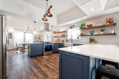 Example of a large country u-shaped medium tone wood floor and brown floor eat-in kitchen design in Other with a farmhouse sink, recessed-panel cabinets, blue cabinets, quartzite countertops, white backsplash, subway tile backsplash, stainless steel appliances, a peninsula and white countertops