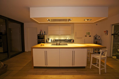 Offene, Zweizeilige, Mittelgroße Moderne Küche mit Unterbauwaschbecken, weißen Schränken, Arbeitsplatte aus Holz, Küchenrückwand in Schwarz, braunem Holzboden und Kücheninsel in Dortmund