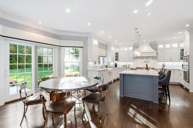 Large transitional u-shaped eat-in kitchen in New York with a farmhouse sink, white cabinets, dark hardwood floors, shaker cabinets, marble benchtops, grey splashback, stone tile splashback, with island and white benchtop.