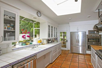 This is an example of a modern eat-in kitchen in Santa Barbara with a double-bowl sink, recessed-panel cabinets, white cabinets, stainless steel appliances, terra-cotta floors, with island and tile benchtops.