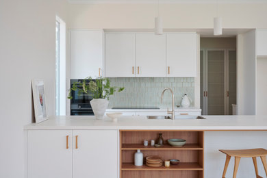 Photo of a modern galley kitchen pantry in Adelaide with a double-bowl sink, flat-panel cabinets, quartz benchtops, green splashback, matchstick tile splashback, stainless steel appliances, light hardwood floors, with island and white benchtop.