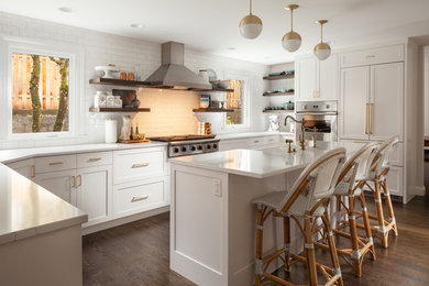 Example of a mid-sized country u-shaped dark wood floor and brown floor open concept kitchen design in Portland with a farmhouse sink, shaker cabinets, white cabinets, quartz countertops, white backsplash, subway tile backsplash, stainless steel appliances and an island