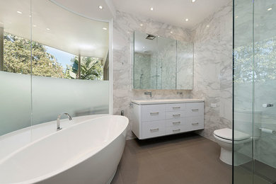 Inspiration for a mid-sized modern master bathroom in Melbourne with a drop-in sink, white cabinets, engineered quartz benchtops, a freestanding tub, an open shower, a one-piece toilet, beige tile, porcelain tile, white walls and porcelain floors.