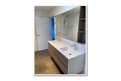 Design ideas for a mid-sized modern master bathroom in Central Coast with recessed-panel cabinets, light wood cabinets, a corner shower, gray tile, ceramic tile, grey walls, ceramic floors, solid surface benchtops, brown floor, a hinged shower door, white benchtops, a double vanity and a freestanding vanity.