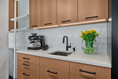 This is an example of an expansive contemporary galley open plan kitchen in Minneapolis with a submerged sink, flat-panel cabinets, black cabinets, engineered stone countertops, white splashback, engineered quartz splashback, integrated appliances, concrete flooring, an island, brown floors and white worktops.