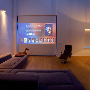 Large minimalist open concept light wood floor and yellow floor home theater photo in Dusseldorf with white walls and a projector screen