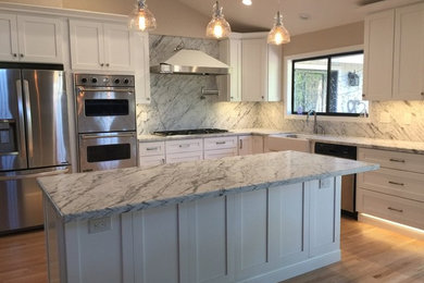 Inspiration for a large contemporary l-shaped kitchen in San Francisco with a farmhouse sink, shaker cabinets, white cabinets, marble benchtops, white splashback, stone slab splashback, stainless steel appliances, light hardwood floors, with island and beige floor.