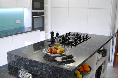 Design ideas for a large modern l-shaped kitchen/diner in Glasgow with a built-in sink, flat-panel cabinets, white cabinets, granite worktops, blue splashback, glass sheet splashback, stainless steel appliances, porcelain flooring and an island.