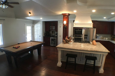 Inspiration for a large country l-shaped brown floor and dark wood floor open concept kitchen remodel in Other with an undermount sink, raised-panel cabinets, distressed cabinets, granite countertops, beige backsplash, ceramic backsplash, stainless steel appliances and an island