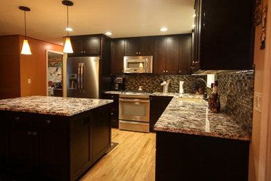 Example of a mid-sized transitional l-shaped light wood floor open concept kitchen design in Portland with an undermount sink, shaker cabinets, brown cabinets, quartz countertops, gray backsplash, glass tile backsplash, stainless steel appliances and an island