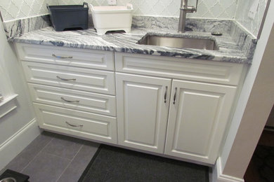 Small elegant porcelain tile utility room photo in Atlanta with an undermount sink, raised-panel cabinets, white cabinets, marble countertops and a stacked washer/dryer
