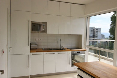 Inspiration for a small modern single-wall ceramic tile and beige floor eat-in kitchen remodel in Other with a double-bowl sink, flat-panel cabinets, white cabinets, wood countertops, white backsplash, ceramic backsplash, stainless steel appliances, an island and brown countertops