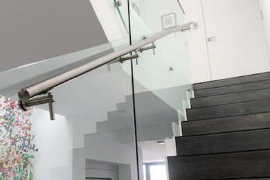 This is an example of a large modern tile u-shaped staircase in Sydney with tile risers, metal railing and brick walls.