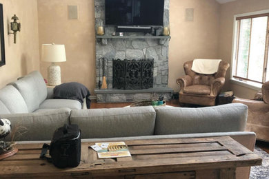 Example of a transitional open concept medium tone wood floor, brown floor and vaulted ceiling family room design in New York with beige walls, a standard fireplace, a stone fireplace and a wall-mounted tv