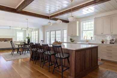 Large country l-shaped medium tone wood floor and exposed beam eat-in kitchen photo in Boston with a farmhouse sink, recessed-panel cabinets, beige cabinets, quartz countertops, beige backsplash, ceramic backsplash, paneled appliances, an island and beige countertops