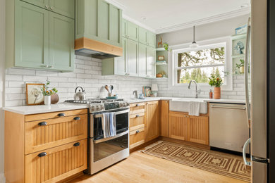 Kitchen - traditional u-shaped light wood floor and beige floor kitchen idea in Portland with a farmhouse sink, shaker cabinets, green cabinets, white backsplash, subway tile backsplash, stainless steel appliances and white countertops