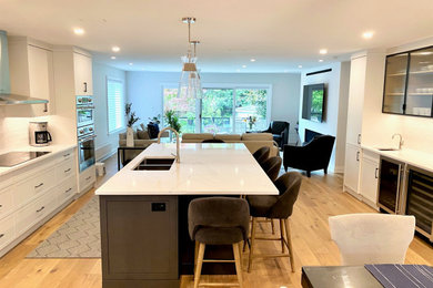 Example of a mid-sized trendy galley light wood floor open concept kitchen design in Toronto with an undermount sink, recessed-panel cabinets, quartz countertops, white backsplash, porcelain backsplash, stainless steel appliances, an island and white countertops