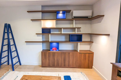 Modelo de sala de estar con biblioteca abierta contemporánea de tamaño medio sin chimenea y televisor con paredes blancas, suelo de madera clara y suelo beige
