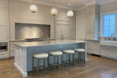 Eat-in kitchen - mid-sized transitional l-shaped medium tone wood floor and brown floor eat-in kitchen idea in DC Metro with a farmhouse sink, shaker cabinets, beige cabinets, quartzite countertops, beige backsplash, marble backsplash, paneled appliances, an island and beige countertops