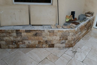 CINDER BLOCKS BECOME A STONE WALL IN A PATIO AREA WITH THIN TRAVENTINE PAVES