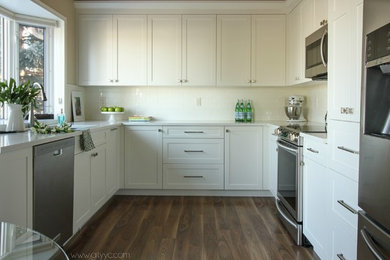 Example of a mid-sized classic u-shaped laminate floor eat-in kitchen design in Calgary with a drop-in sink, shaker cabinets, white cabinets, quartzite countertops, white backsplash, ceramic backsplash, stainless steel appliances and no island