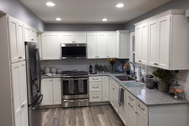 Example of a mid-sized classic u-shaped vinyl floor and gray floor eat-in kitchen design in DC Metro with an undermount sink, flat-panel cabinets, white cabinets, quartz countertops, white backsplash, ceramic backsplash and stainless steel appliances