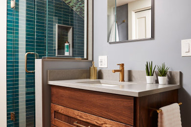 Transitional 3/4 green tile medium tone wood floor, brown floor and single-sink alcove shower photo in Minneapolis with shaker cabinets, medium tone wood cabinets, gray walls, an undermount sink, quartz countertops, gray countertops and a built-in vanity