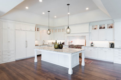 Expansive transitional l-shaped open plan kitchen in Philadelphia with an undermount sink, raised-panel cabinets, white cabinets, marble benchtops, white splashback, subway tile splashback, panelled appliances, medium hardwood floors, with island and brown floor.