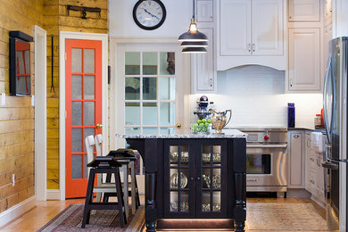 Example of a mid-sized transitional u-shaped medium tone wood floor and brown floor eat-in kitchen design in Other with a farmhouse sink, raised-panel cabinets, white cabinets, granite countertops, white backsplash, subway tile backsplash, stainless steel appliances, an island and multicolored countertops