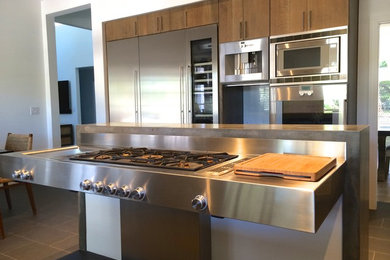 Inspiration for a mid-sized contemporary porcelain tile enclosed kitchen remodel in Phoenix with flat-panel cabinets, medium tone wood cabinets, stainless steel countertops, gray backsplash, metal backsplash, stainless steel appliances and an island