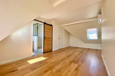 Aménagement d'une grande chambre mansardée ou avec mezzanine contemporaine avec un mur blanc, parquet clair et un sol marron.