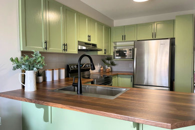 Enclosed kitchen - contemporary l-shaped ceramic tile and beige floor enclosed kitchen idea in Ottawa with a drop-in sink, shaker cabinets, green cabinets, wood countertops, white backsplash, matchstick tile backsplash, stainless steel appliances, a peninsula and brown countertops