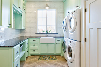 Dedicated laundry room - country u-shaped ceramic tile and gray floor dedicated laundry room idea in Oklahoma City with a farmhouse sink, shaker cabinets, green cabinets, granite countertops, white walls and a stacked washer/dryer