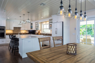 Example of a mid-sized trendy l-shaped dark wood floor open concept kitchen design in Miami with a farmhouse sink, shaker cabinets, white cabinets, granite countertops, beige backsplash, matchstick tile backsplash, stainless steel appliances and an island